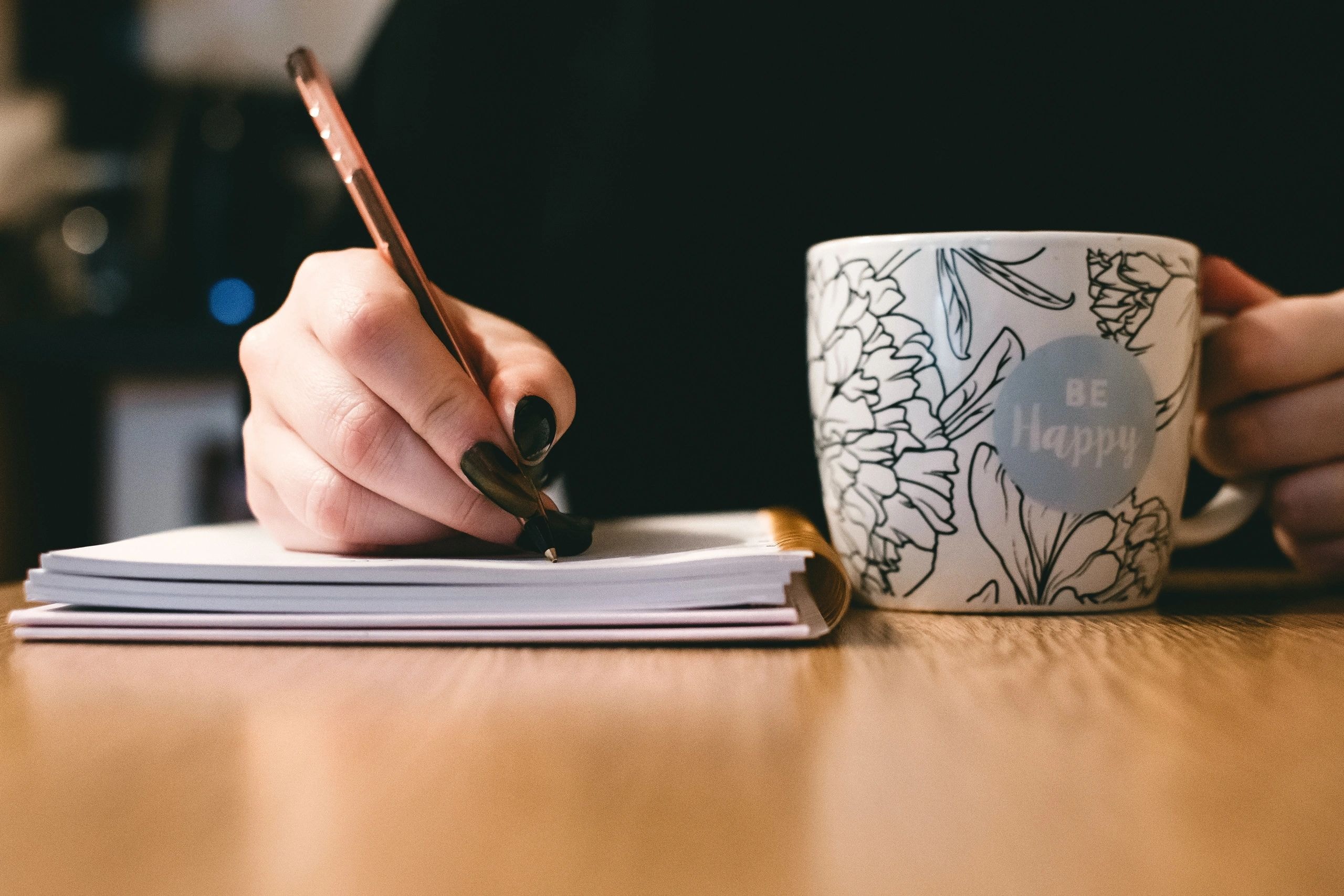 Person writing in a notebook with a coffee mug